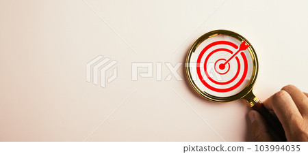 A magnifier glass highlights a target board for focused business objectives. With a background and copy space, it symbolizes the concept of search, goal achievement, and successful strategies. A magnifier glass highlights a target board for focused business objectives. With a background and copy space, it symbolizes the concept of search, goal achievement, and successful strategies. 103994035