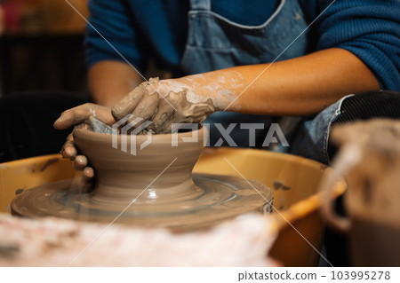 Close up on skillful hands sculpting pottery jar on potter wheel Close up on skillful hands sculpting pottery jar on potter wheel 103995278