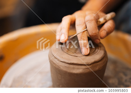 Close up on skillful hands sculpting pottery jar on potter wheel Close up on skillful hands sculpting pottery jar on potter wheel 103995803