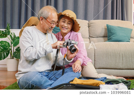 Senior woman holding digital camera taking photos of husband at home 103996081
