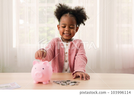 Little girl putting coin of cash into ceramic piggy bank 103996114