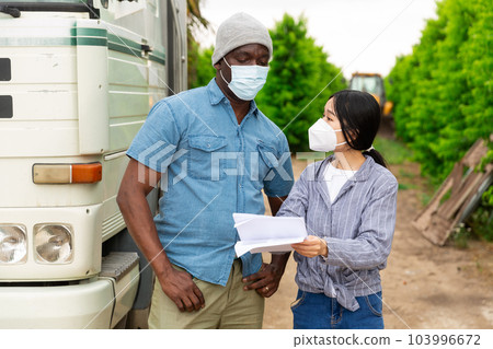 Farmer and woman in masks signing documents near truck at orchard Farmer and woman in masks signing documents near truck at orchard 103996672