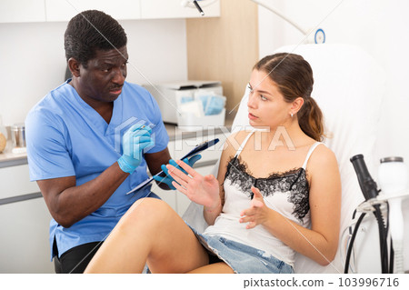 Cosmetician talking with young woman before procedure Cosmetician talking with young woman before procedure 103996716