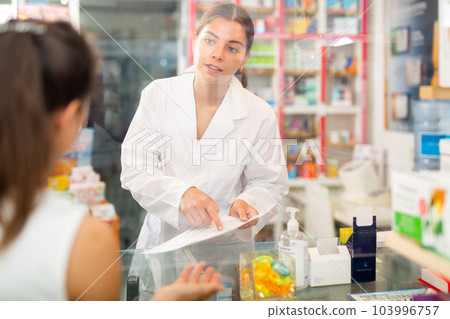 Young female pharmacist is studying a prescription for a medicine brought by a customer 103996757