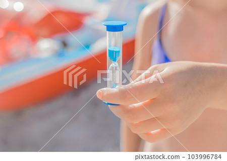 The girl's hand holds a close-up hourglass. The concept of leaky time The girl's hand holds a close-up hourglass. The concept of leaky time 103996784