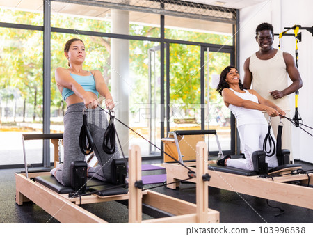 Woman performing set of pilates exercises on reformer in modern fitness studio 103996838