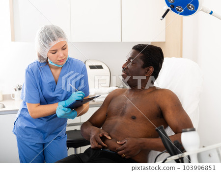 Woman cosmetician consulting man before cosmetological body treatment Woman cosmetician consulting man before cosmetological body treatment 103996851