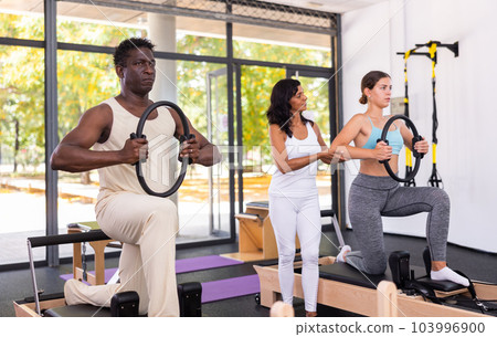 Man and woman doing exercises in pilates gym with man instructor Man and woman doing exercises in pilates gym with man instructor 103996900