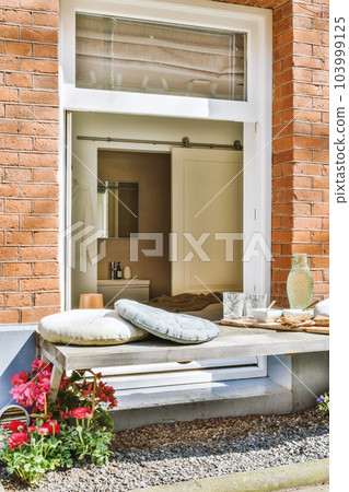 an outside area with flowers and pillows on the window sies, in front of a brick building that is being used as a an outside area with flowers and pillows on the window sies, in front of a brick building that is being used as a 103999125