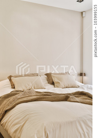 a bed with pillows and blankets on it in a room that has white walls, wood flooring and large windows 103999155