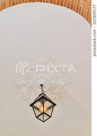 a light hanging on the side of a brick wall in a room with white walls and an ornate design above it 103999177