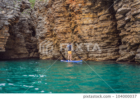 Young men Having Fun Stand Up Paddling in blue water seaamong the rocks in Montenegro. SUP 104000037