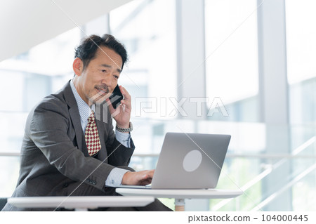 Middle-aged businessman (boss, president, leader) talking on a smartphone in the office Middle-aged businessman (boss, president, leader) talking on a smartphone in the office 104000445