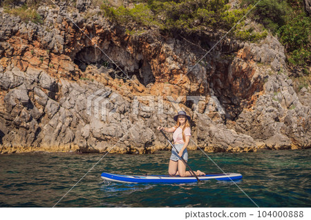 Young women Having Fun Stand Up Paddling in blue water seaamong the rocks in Montenegro. SUP 104000888