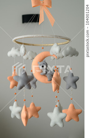 Baby crib mobile hanging in the nursery room, orange and grey pastel-colored theme, sleeping bear on the moon surrounded with stars. Baby crib mobile hanging in the nursery room, orange and grey pastel-colored theme, sleeping bear on the moon surrounded with stars. 104001204
