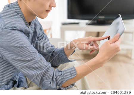 Young man operating a tablet in the living room at home Young man operating a tablet in the living room at home 104001289