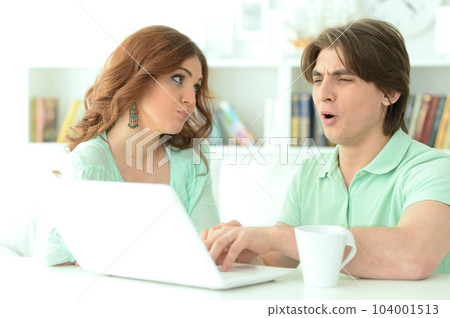Portrait of happy young couple looking at laptop while drinking tea at home Portrait of happy young couple looking at laptop while drinking tea at home 104001513