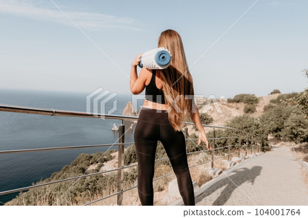 Fitness woman sea. Outdoor workout on yoga mat roller in park near to ocean beach. Female fitness pilates yoga routine concept. Healthy lifestyle. Happy fit woman exercising with rubber band in park. 104001764