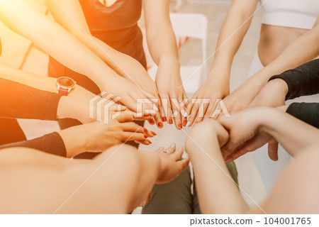 Partnership and unity concept: unrecognizable women in sportswear holding wrists of each other, forming circle. Group of happy young womans holding hands. Side view on human hands. Selective focus 104001765