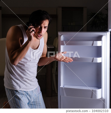 Man breaking diet at night near fridge Man breaking diet at night near fridge 104002310