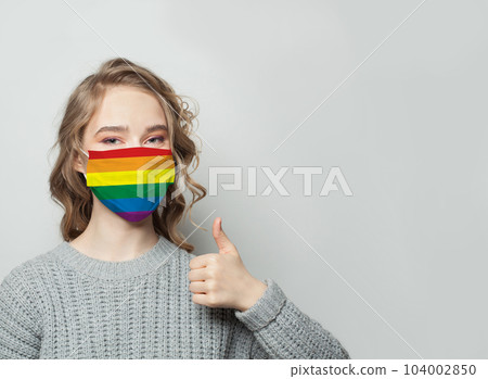 Happy woman in face mask with LGBT flag holding thumb up. LGBT medicine, unity, protecion concept 104002850