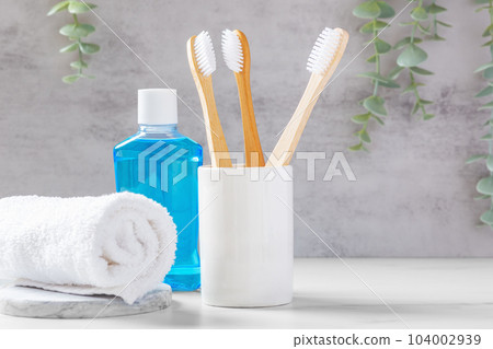 Bamboo toothbrushes in white cup with mouthwash and towel, dental care background Bamboo toothbrushes in white cup with mouthwash and towel, dental care background 104002939