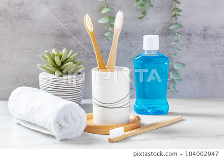 Dental care and dental hygiene concept, bamboo toothbrushes in cup with mouthwash and towel Dental care and dental hygiene concept, bamboo toothbrushes in cup with mouthwash and towel 104002947