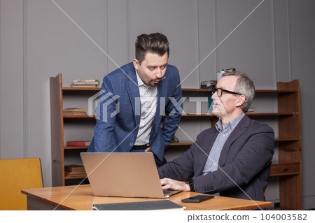 Mature businessman in blue suit and his younger colleague are thinking about business plans 104003582