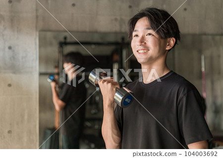 亞洲男子在健身房用啞鈴和鐵陣列進行肌肉訓練以加強手臂 104003692