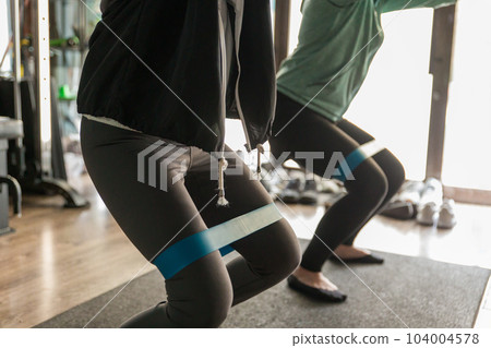 Athlete woman doing squats with training tube in gym 104004578