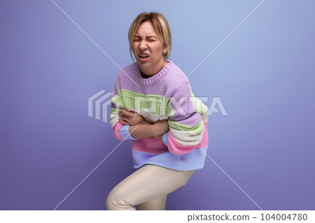 blond girl is experiencing discomfort in the abdomen on a purple background with copy space 104004780