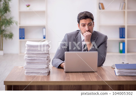 Young male employee and too much work in the office 104005302