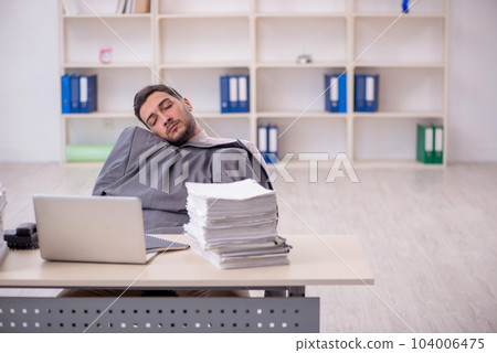 Young male employee unhappy with excessive work in the office Young male employee unhappy with excessive work in the office 104006475