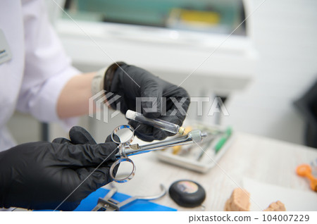 Close-up dentist hands placing a cartridge with dental anesthesia in a stainless steel syringe, preparing the anesthetic procedure at dental clinic. Dentistry. Orthodontics. Maxillofacial surgery Close-up dentist hands placing a cartridge with dental anesthesia in a stainless steel syringe, preparing the anesthetic procedure at dental clinic. Dentistry. Orthodontics. Maxillofacial surgery 104007229