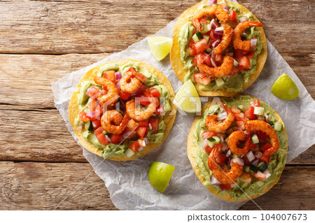 Crispy tostadas topped with guacamole, spiced shrimp, and fresh salsa closeup on the table. Horizontal top view Crispy tostadas topped with guacamole, spiced shrimp, and fresh salsa closeup on the table. Horizontal top view 104007673