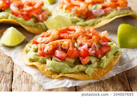 Freshly made shrimp tostadas topped with guacamole, onion, tomatoes, and cucumbers closeup on the table. Horizontal Freshly made shrimp tostadas topped with guacamole, onion, tomatoes, and cucumbers closeup on the table. Horizontal 104007685