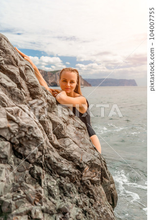 Woman swimsuit sea. Attractive blonde woman in a black swimsuit enjoying the sea air on the seashore around the rocks. Travel and vacation concept. 104007755