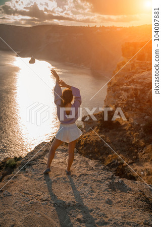 Free girl with open arms at sunset over the sea, sun over clouds Free girl with open arms at sunset over the sea, sun over clouds 104007881