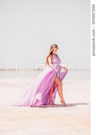 Woman pink salt lake. Against the backdrop of a pink salt lake, a woman in a long pink dress takes a leisurely stroll along the white, salty shore, capturing a wanderlust moment. Woman pink salt lake. Against the backdrop of a pink salt lake, a woman in a long pink dress takes a leisurely stroll along the white, salty shore, capturing a wanderlust moment. 104007888