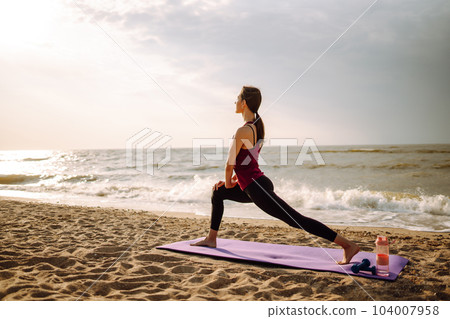 Young woman in sportswear doing yoga, fitness exerciseon the beach. Sport, Active life. 104007958