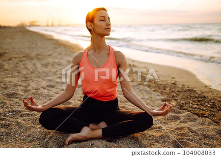 Young beautiful woman practices yoga and meditates on the beach. Sport, Active life. 104008033