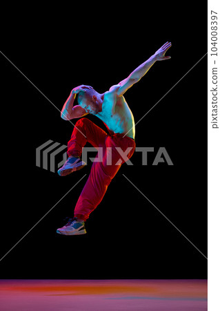Young muscular man with relief shirtless body dancing breakdance against black studio background in neon light 104008397