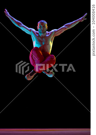 Freedom of movements. Young muscular guy, street dancer performing, dancing breakdance against black studio background in neon light 104008416