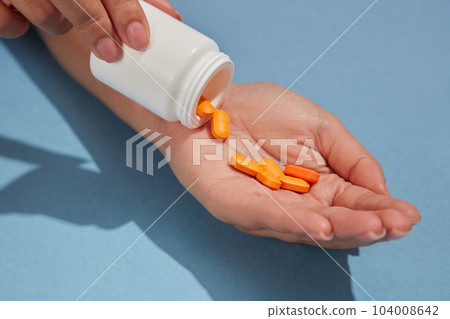 Against the blue background, orange pills are poured from a white bottle unlabeled into a woman's palm. View from above, advertising scene 104008642