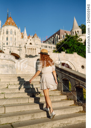 Happy young woman in hat at dawn enjoys view of beautiful buildings. Lifestyle, recreation concept. 104008948