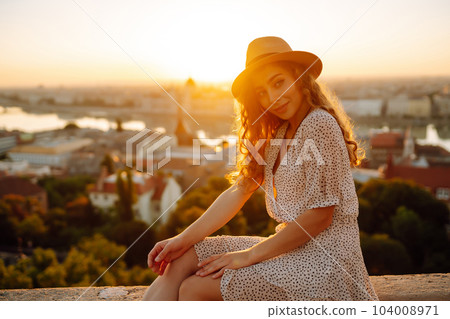 Portrait of happy tourist in hat at dawn enjoys cityscape. Traveling in Europe. Concept tourism. 104008971