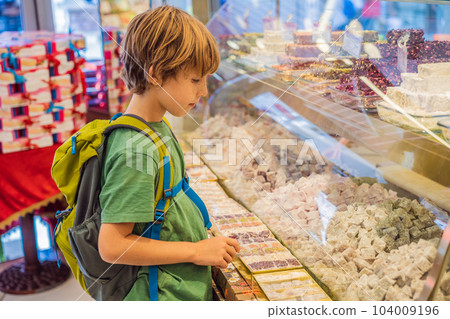 The boy looks at the counter with Turkish sweets. Traditional oriental sweet pastry cookies, nuts, dried fruits, pastilles, marmalade, Turkish desert with sugar, honey and pistachio, in display at a The boy looks at the counter with Turkish sweets. Traditional oriental sweet pastry cookies, nuts, dried fruits, pastilles, marmalade, Turkish desert with sugar, honey and pistachio, in display at a 104009196
