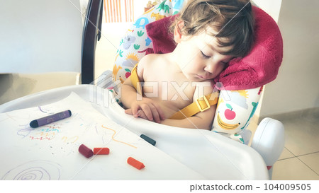 A little baby boy toddler asleep in his high-chair after playing with colored crayons 104009505