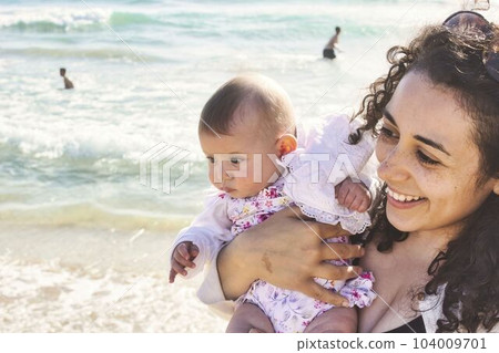 Young mother and daughter baby girl looking happy at the beach 104009701
