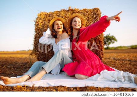 Two smiling young woman resting near haystack. Fashion concept. Nature, vacation, relax and lifestyle. 104010169